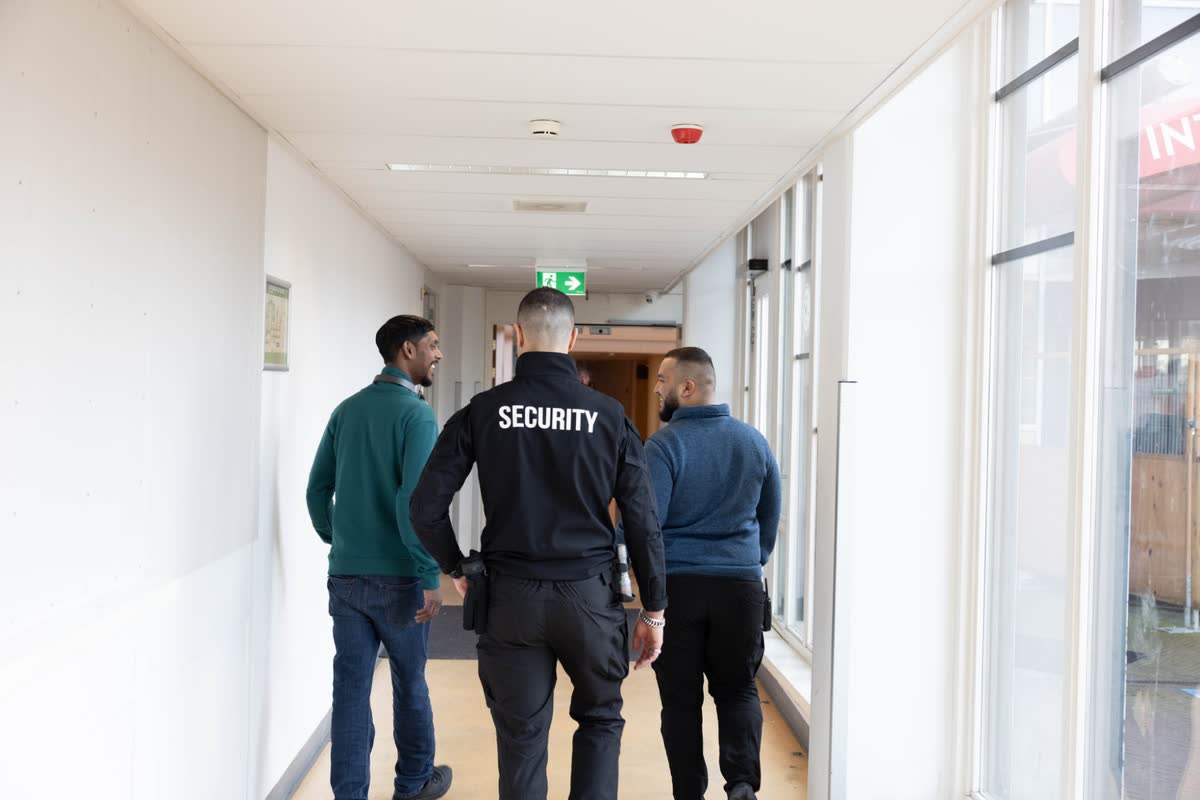 Beveiliger van Adaptive Safety Solutions loopt met twee bezoekers door een gang